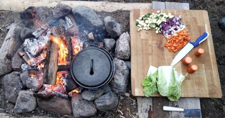 A fire, a pot, and some ingredients on a cutting board.